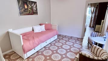 Ein Zimmer mit einem Bett, einem Sessel, einem gemusterten Boden, einem Gemälde und einer Pendelleuchte.