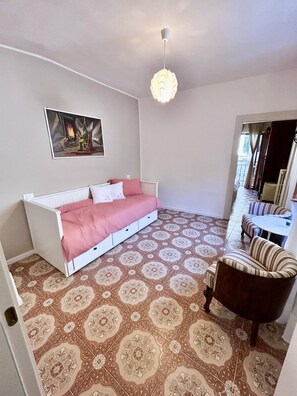 A room with a bed, a chair, a patterned floor, a painting, and a hanging light fixture.