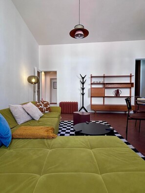 A modern living room with a green sofa, a black and white checkered rug, a wooden bookshelf, and a floor lamp. - Piazza Condo - InBorgo (ACQUASPARTA)