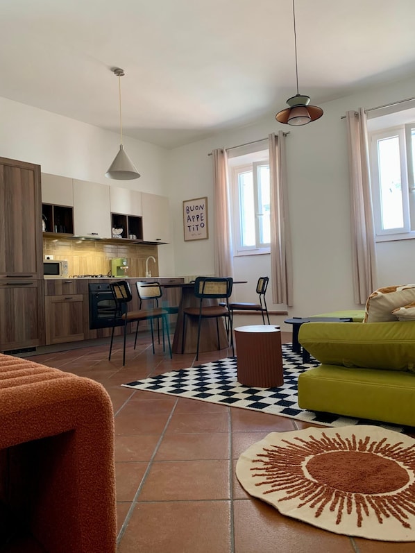 Un salon moderne avec un canapé vert, une table basse et un coin cuisine doté de meubles en bois et d’une table à manger.