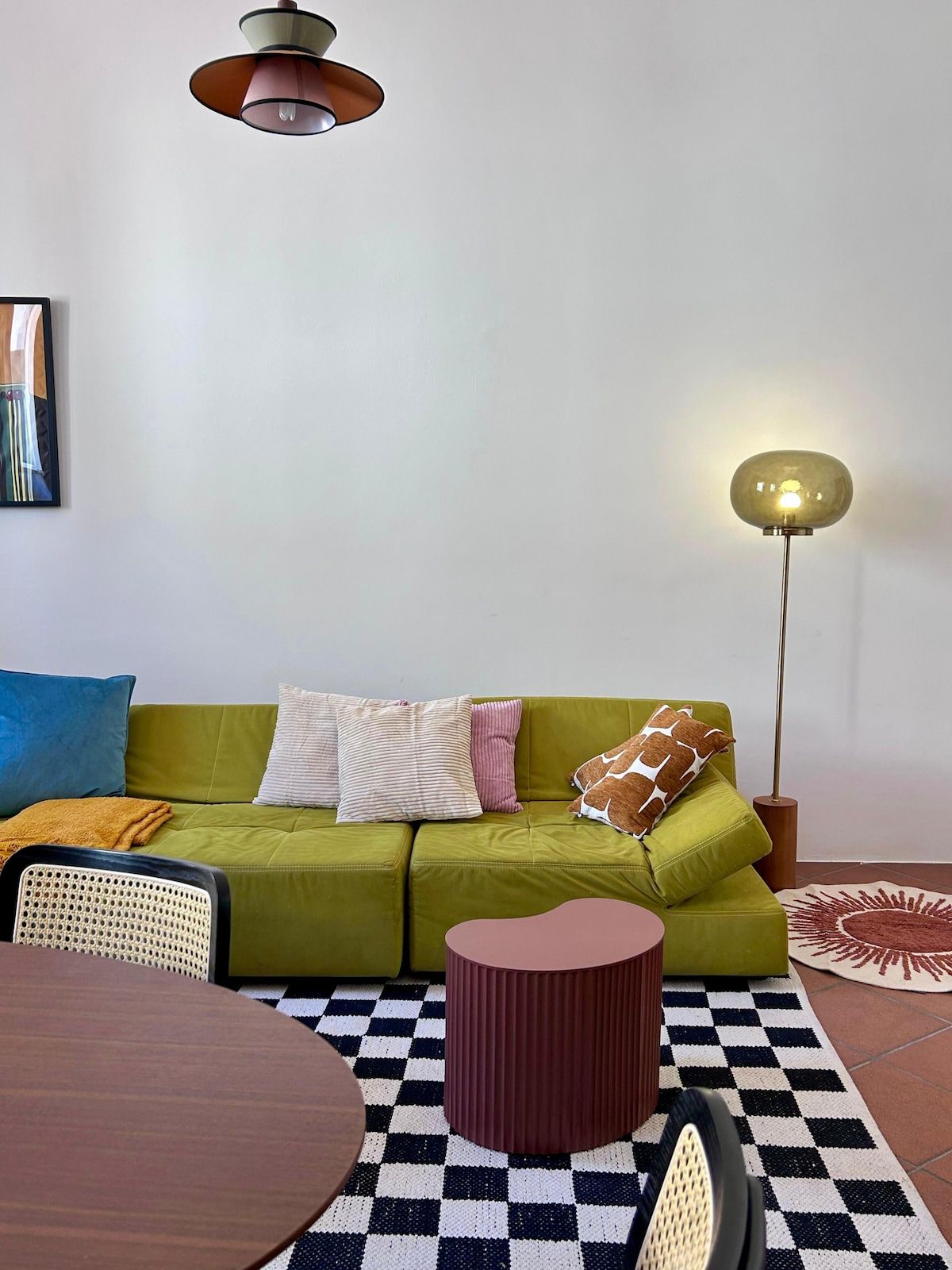 Un divano verde con cuscini, un tavolino rotondo, un pavimento a scacchi, una lampada da terra alta e un quadro appeso al muro.