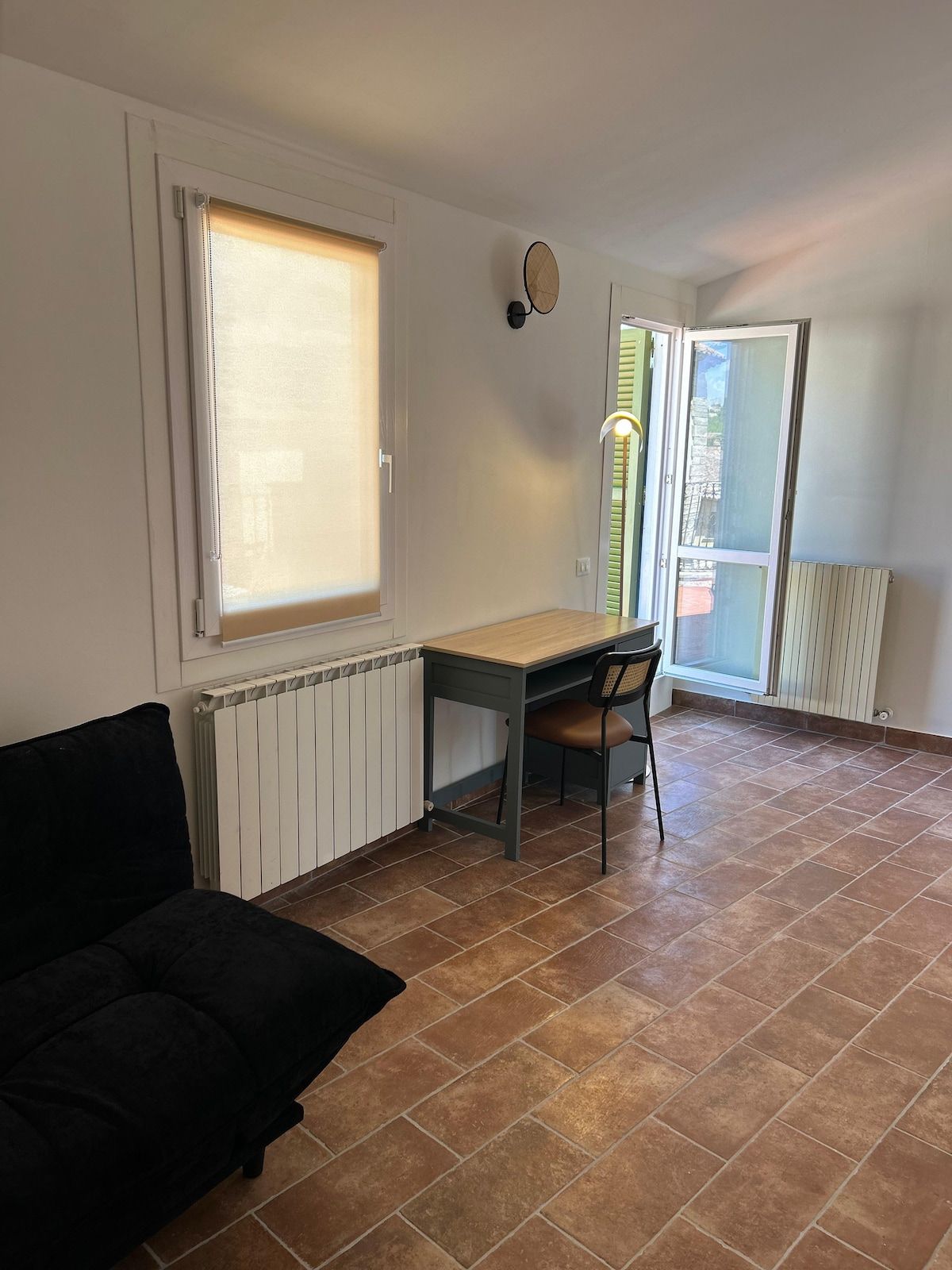 A room with a desk, chair, radiator, and a black sofa.