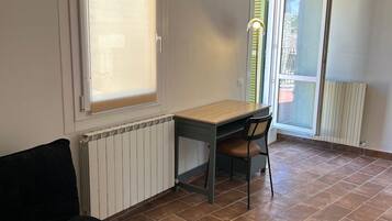 A room with a desk, chair, radiator, and a black sofa.
