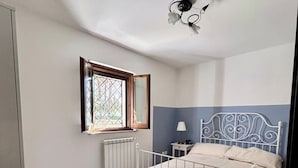A bedroom with a bed, a window, a radiator, a ceiling fan, and a blue patterned rug.