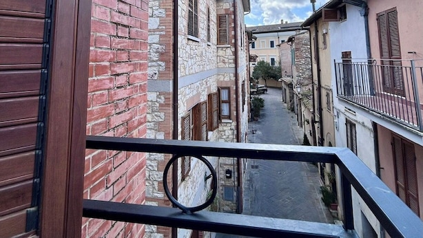 A narrow street with buildings on either side, a clear sky, and a balcony railing.