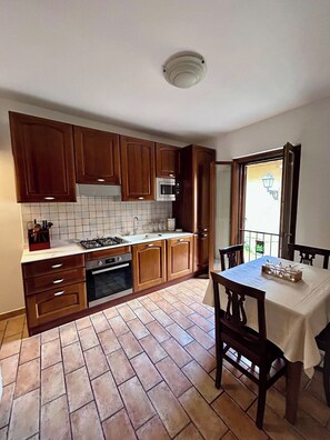 Una cocina con armarios de madera, estufa a gas, horno y comedor con mesa y sillas.