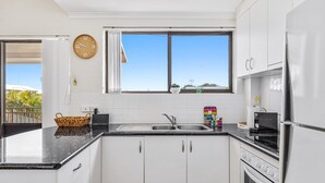 Una cocina moderna con gabinetes blancos, encimera negra, horno empotrado y una ventana con vistas al cielo.