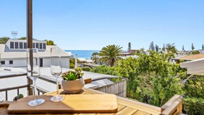 A balcony with a table set for two, overlooking a coastal area with buildings and greenery. - Quaint 2-bed Beach Abode With Ocean Views (Sunshine Coast)