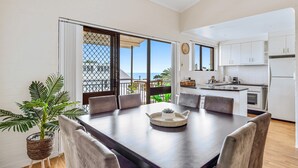 Una cocina moderna con armarios blancos y una zona de comedor con una mesa de madera oscura y sillas grises.
