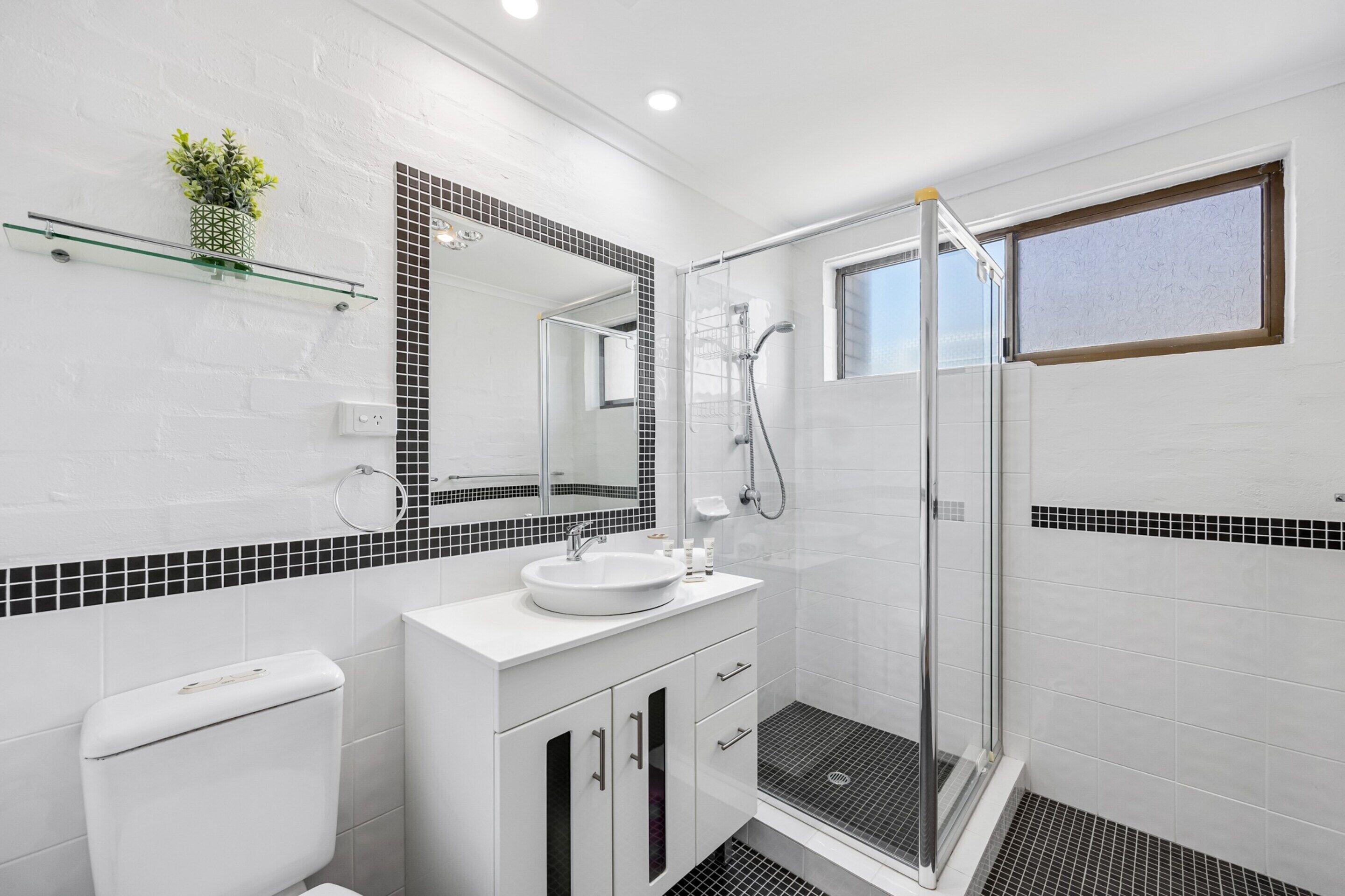Un baño moderno con cabina de ducha de vidrio, un lavabo blanco y un inodoro.