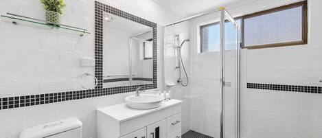 Un baño moderno con cabina de ducha de vidrio, un lavabo blanco y un inodoro.