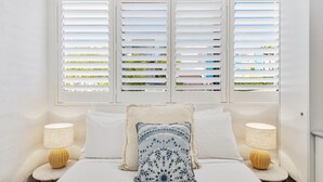 Un dormitorio con una cama, dos mesitas de noche con lámparas y una ventana con persianas.