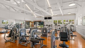 Une salle de sport spacieuse, dotée de divers appareils d’exercice, de grandes fenêtres et d’un plafond haut.