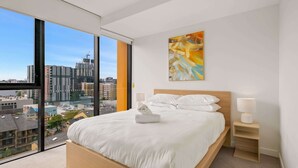 Une chambre moderne avec un grand lit, une vue sur la ville et un tableau accroché au mur.