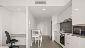 Une cuisine moderne avec des meubles blancs, un coin repas avec une table et des chaises blanches, et un fauteuil de bureau noir.