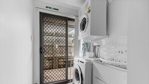Une buanderie équipée d’un lave-linge et d’un sèche-linge, une porte métallique et une vue sur une terrasse en bois à l’extérieur.