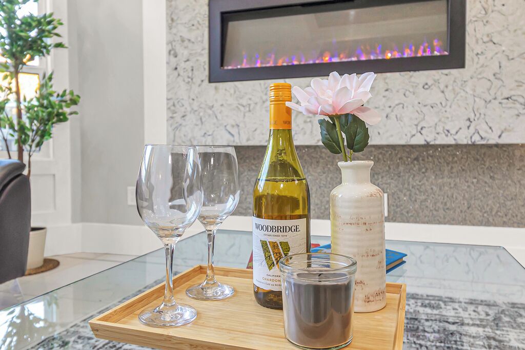 A glass table with a bottle of Woodbridge wine, a candle, and a vase with a pink flower.