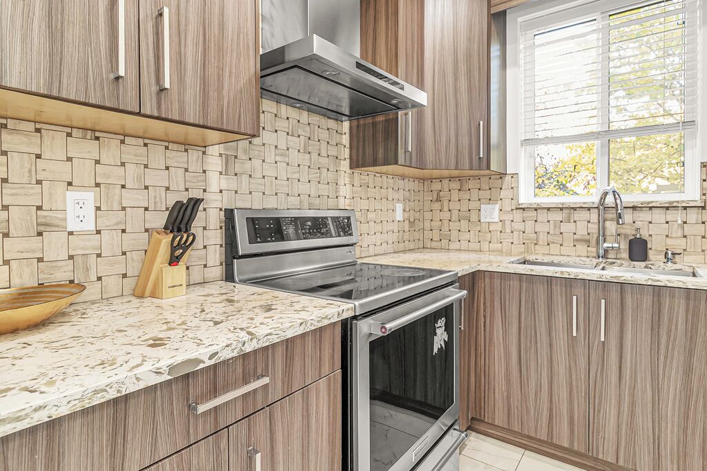 A modern kitchen with wooden cabinets, a built-in stove, and a window with blinds.