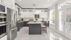 A modern kitchen with stainless steel appliances, a central island, and large windows.