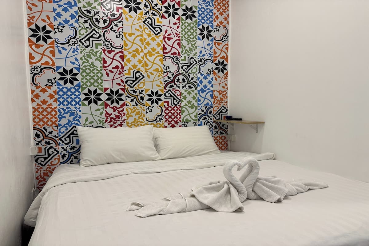 A hotel room with a bed, white bedding, and a colorful patterned headboard.