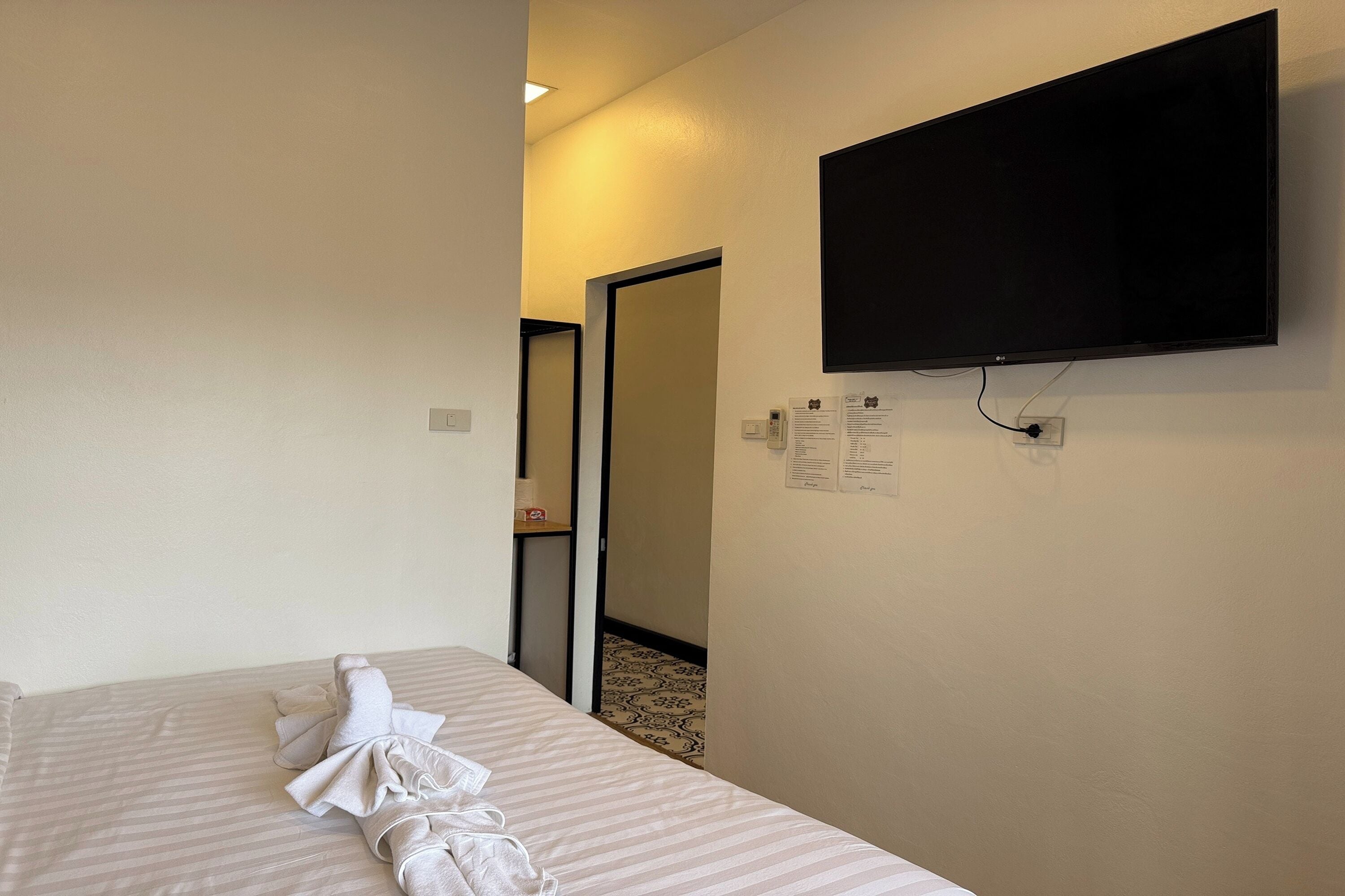 Habitación de hotel con una cama, un televisor de pantalla plana montado en la pared y una puerta que da a otra habitación.