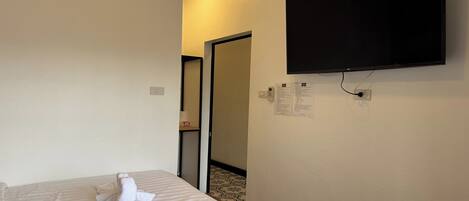 Habitación de hotel con una cama, un televisor de pantalla plana montado en la pared y una puerta que da a otra habitación.