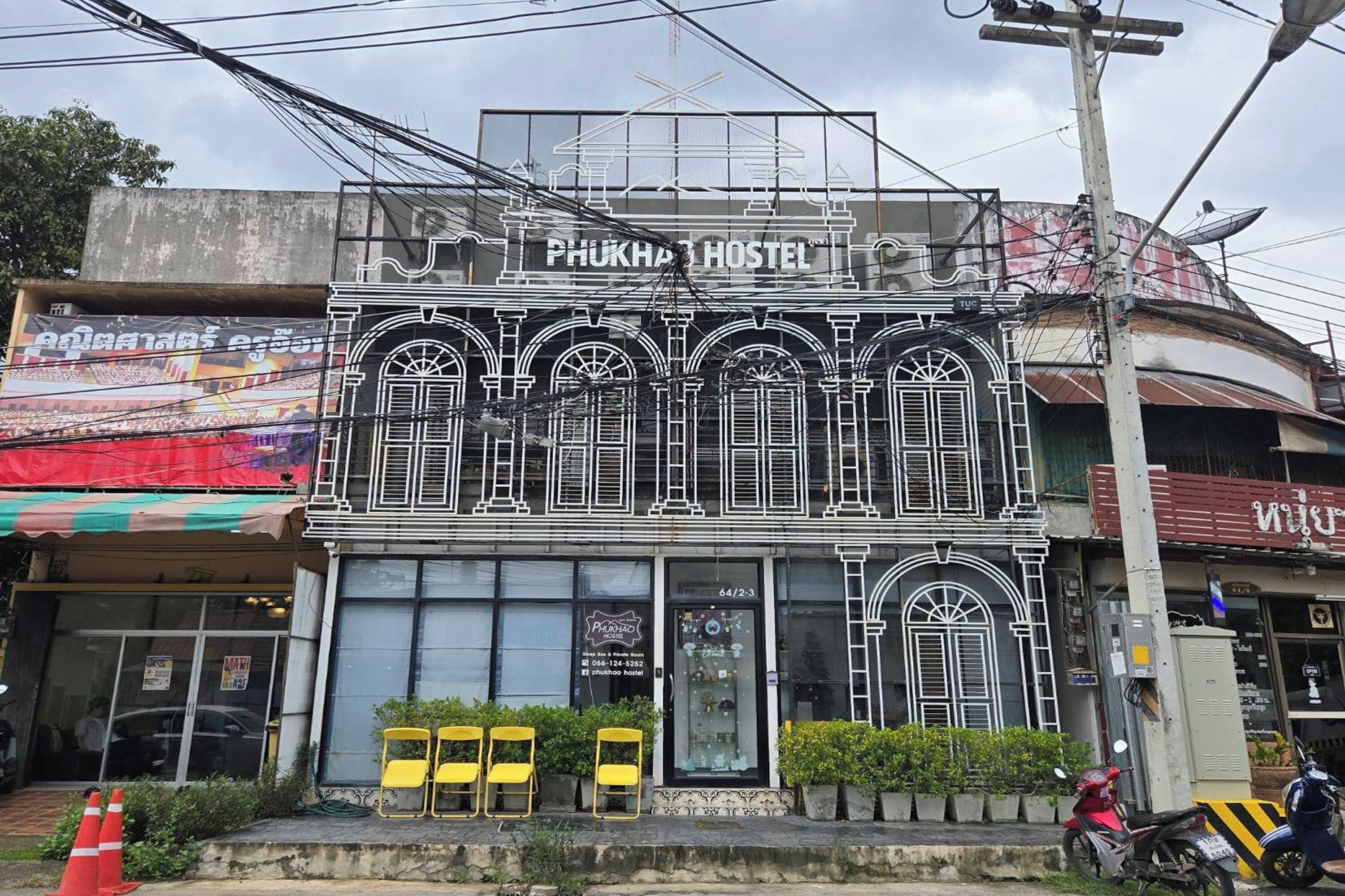 A hostel named "PHUKHA HOSTEL" with a distinctive architectural facade, large windows, and a visible entrance.