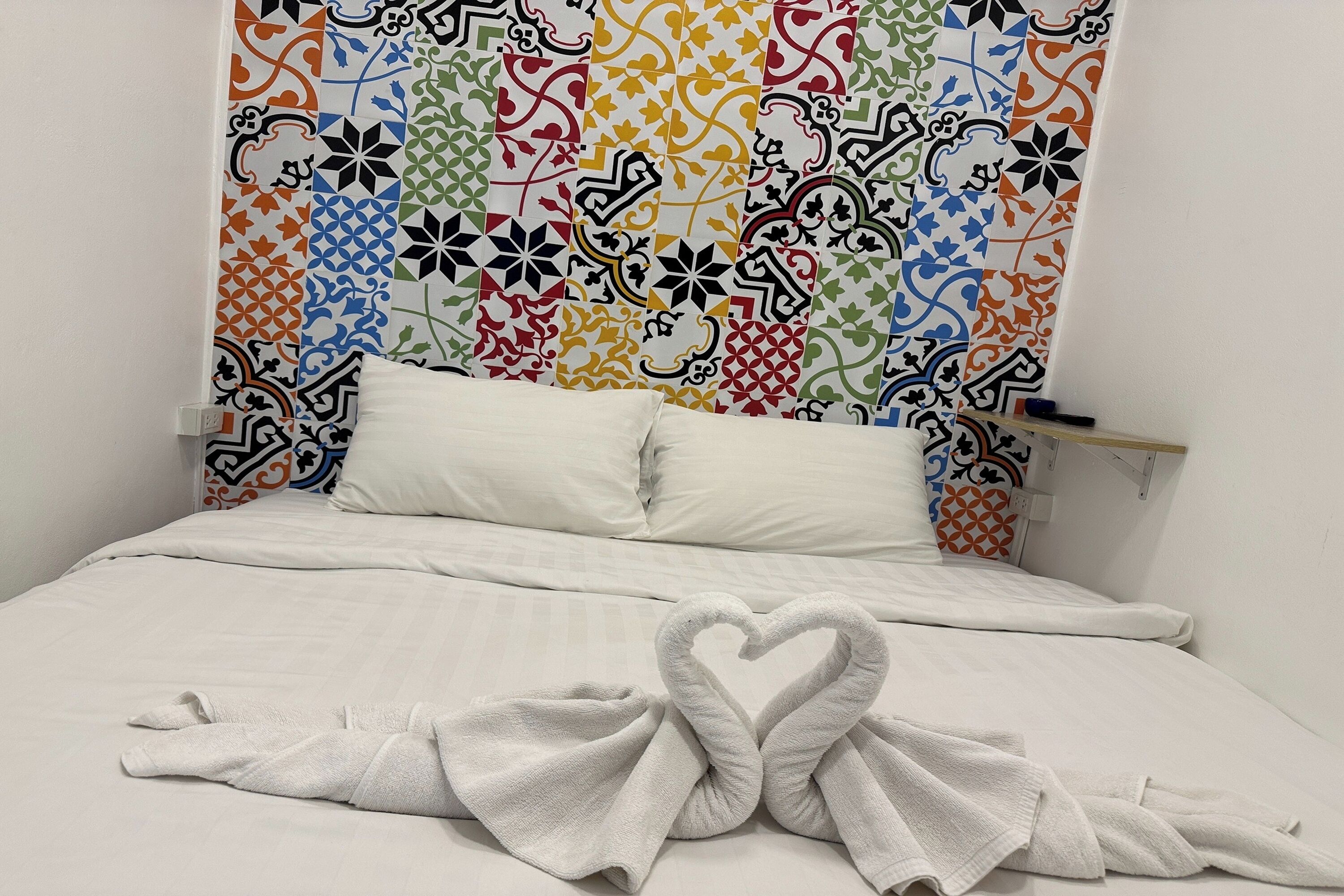 A hotel room with a bed, white bedding, and a colorful patterned headboard.