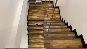 A staircase with wooden steps and metal handrails, leading to a landing with a shelf containing various items. - Phukhao Hostel (Chiang Mai)
