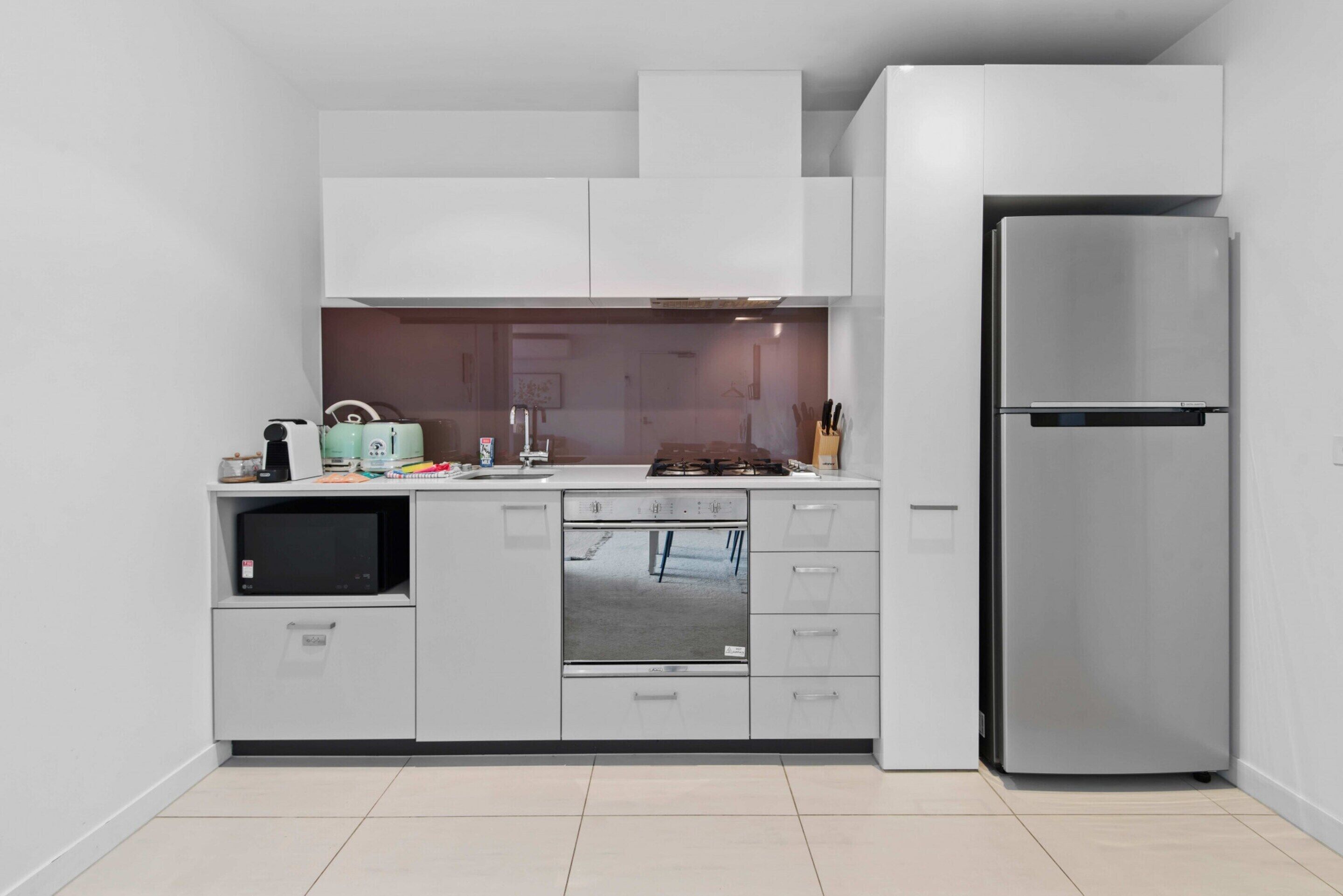 Una cocina moderna con armarios blancos, un refrigerador de acero inoxidable, un microondas y un lavavajillas.