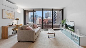 A modern living room with a sofa, coffee table, and TV stand. - Modern 1-bed City Apartment With Pool and Gym (Melbourne)