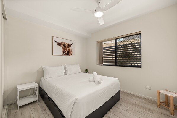 A bedroom with a bed, a ceiling fan, a window with blinds, a small table, and a picture on the wall. - Central South Brisbane Stay With Pool Access (Brisbane)
