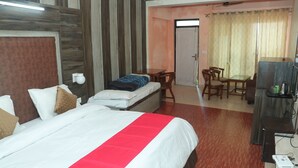 A hotel room with a bed, a desk, a chair, a television, and a door leading to a balcony. - Krishna Hotel And Restaurant (Dharamshala)