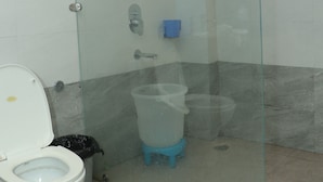 A bathroom with a glass-enclosed shower, a toilet, and a trash bin. - Krishna Hotel And Restaurant (Dharamshala)