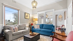 A living room with a grey sofa, a blue sofa, a wooden coffee table, and a red armchair. There is a window with a view of trees and a lamp on a side table. - Bright 3-bed House With Garden, (Blackheath)