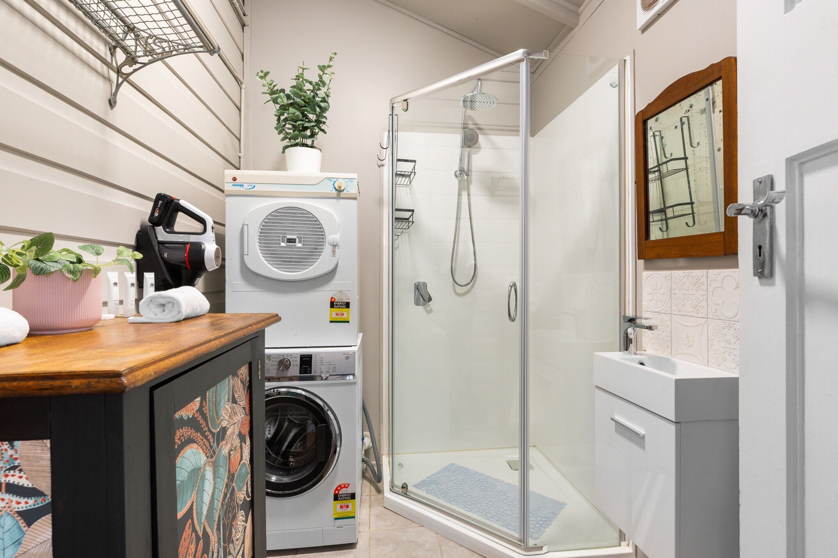 Un espace buanderie comprenant un lave-linge, un sèche-linge et une cabine de douche en verre.