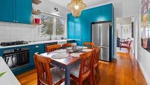 A modern kitchen with teal cabinets, a wooden dining table with chairs, and a stainless steel refrigerator. - Bright 3-bed House With Garden, (Blackheath)
