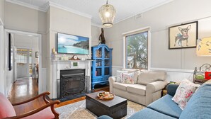A living room with a fireplace, a blue cabinet, a beige sofa, and a television. - Bright 3-bed House With Garden, (Blackheath)