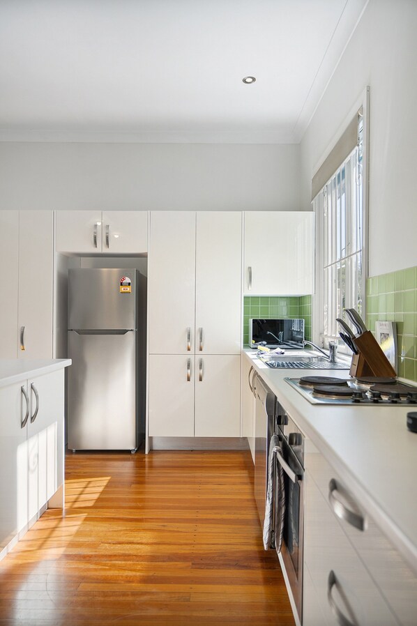 A modern kitchen with white cabinets, a stainless steel refrigerator, a sink, and a window with green-tiled walls.