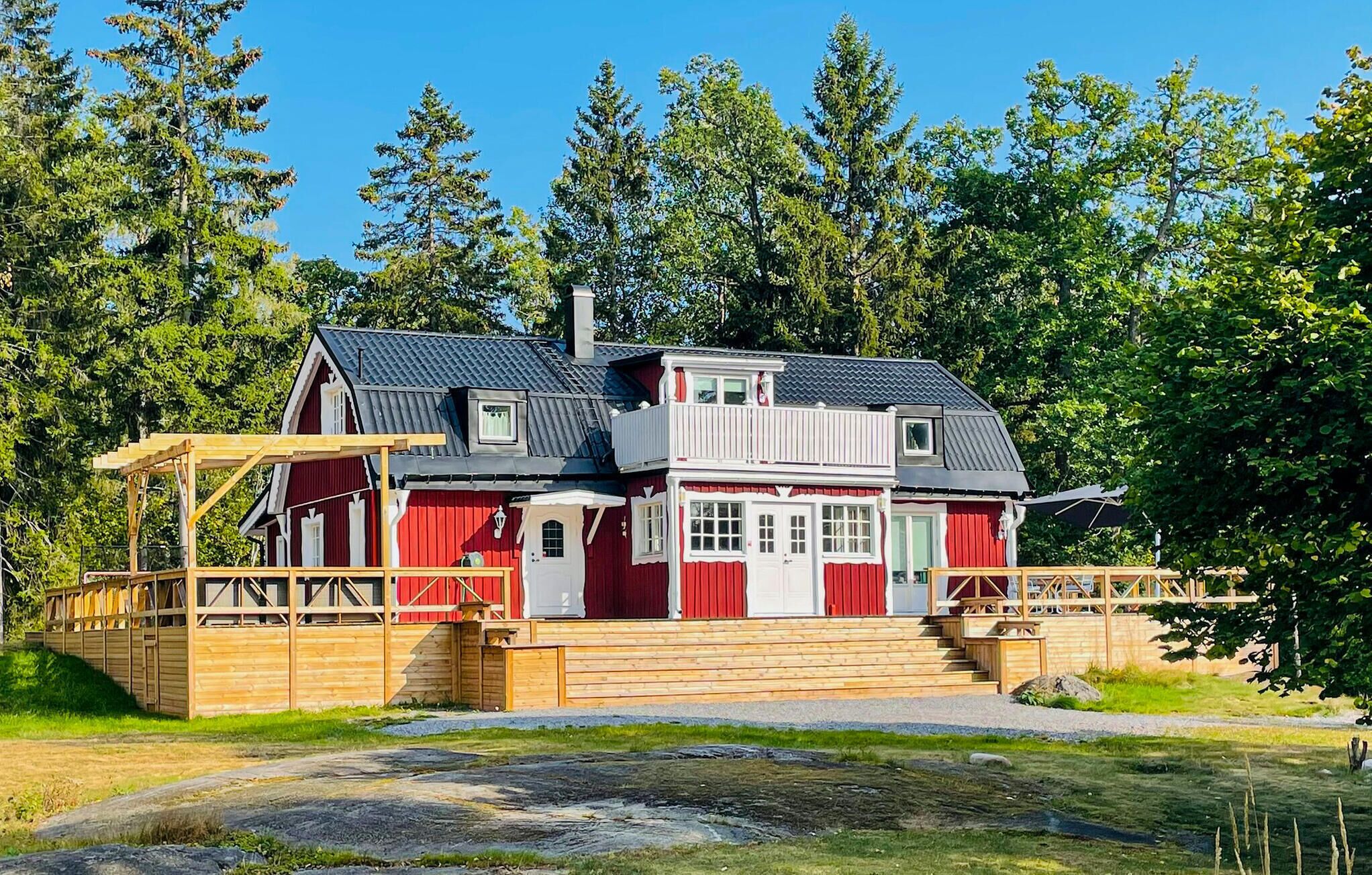 A two-story wooden house with a red and white exterior, a balcony, and a wooden deck.