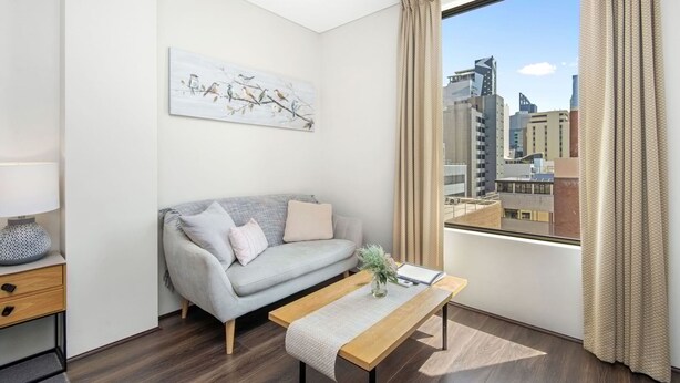 A modern living room with a grey sofa, a wooden coffee table, and a view of the city through large windows. - An Oasis in the City - Studio - by Sepal Stays (Perth)