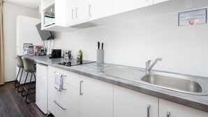 A modern kitchen with white cabinets, a stainless steel sink, and a microwave. There are bar stools and a coffee machine on the counter. - An Oasis in the City - Studio - by Sepal Stays (Perth)