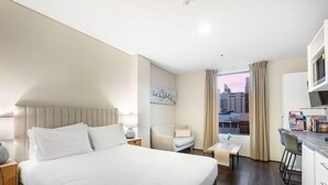 A hotel room with a large bed, a desk, a chair, and a view of the cityscape. - An Oasis in the City - Studio - by Sepal Stays (Perth)