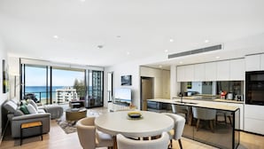 A modern apartment with a dining area, kitchen, and a large window overlooking the sea. - Glorious Ocean Views, 2-bed, Pool & Amenities (Gold Coast)