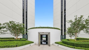 A modern building with a central entrance framed by two tall structures, surrounded by neatly trimmed hedges and a few trees. - Glorious Ocean Views, 2-bed, Pool & Amenities (Gold Coast)