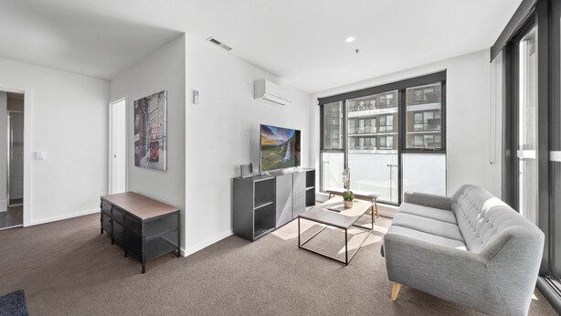 Una sala de estar moderna con un sofá gris, una mesa de centro, un televisor y una estantería.