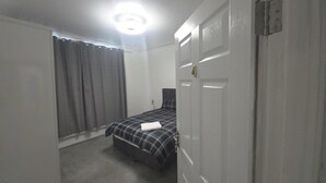 Un dormitorio con cama, puerta y ventana con cortinas.
