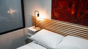 Ein modernes Schlafzimmer mit einem Holzkopfteil, einem Nachttisch mit Lampe und einem großen abstrakten Gemälde an der Wand.