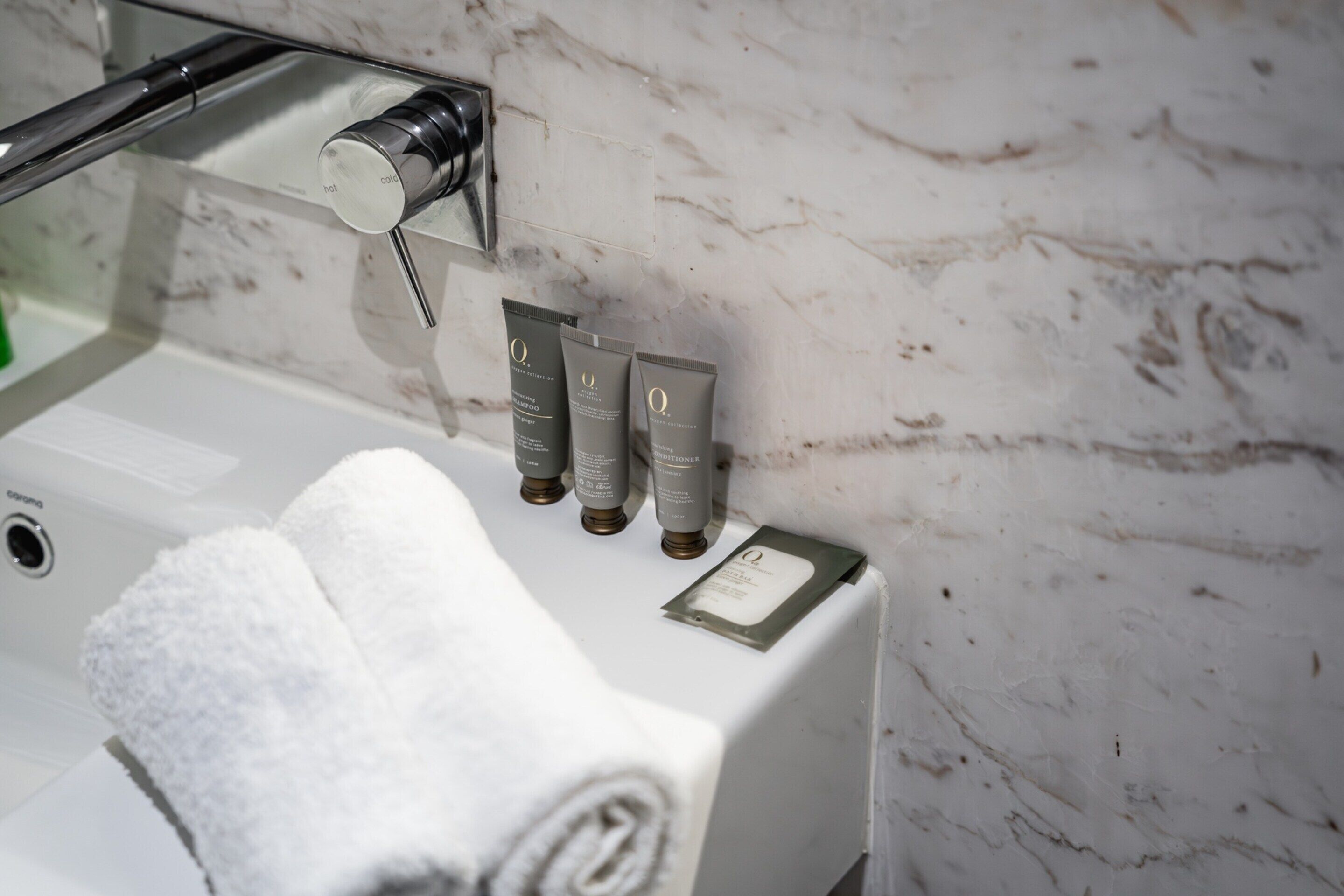 A bathroom with a marble wall, a towel, and three skincare tubes on a counter.