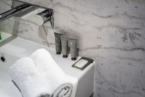 A bathroom with a marble wall, a towel, and three skincare tubes on a counter. - Nott's Nook- 1-bed With Rooftop Views (Melbourne)